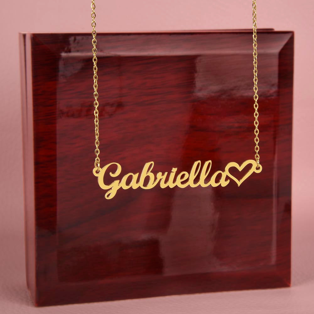 Heart Name Necklace for Myself – A Meaningful Gift for Yourself | gold finish name necklace with heart detail hanging against pink background