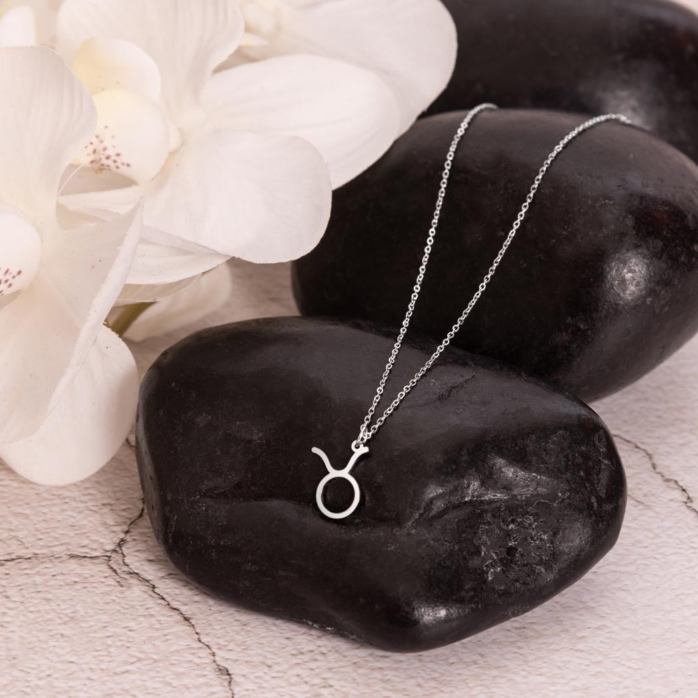 Taurus Zodiac Necklace for Women – Astrology Gift displayed on black stone with white flowers, a meaningful jewelry gift idea