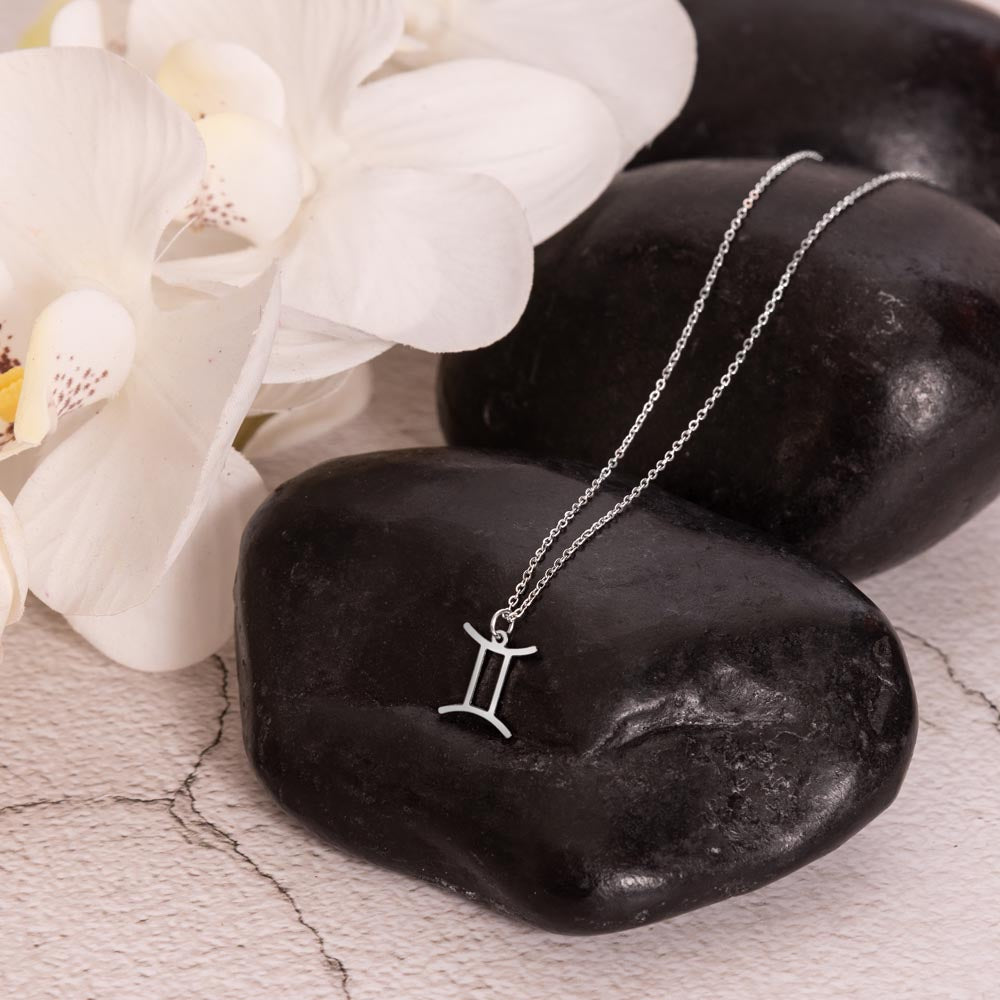 Gemini Zodiac Symbol Necklace for Girls – A Meaningful Gift for a Gemini Girl | Stainless Steel or 18k Yellow Gold Finish displayed on black stones with white flowers