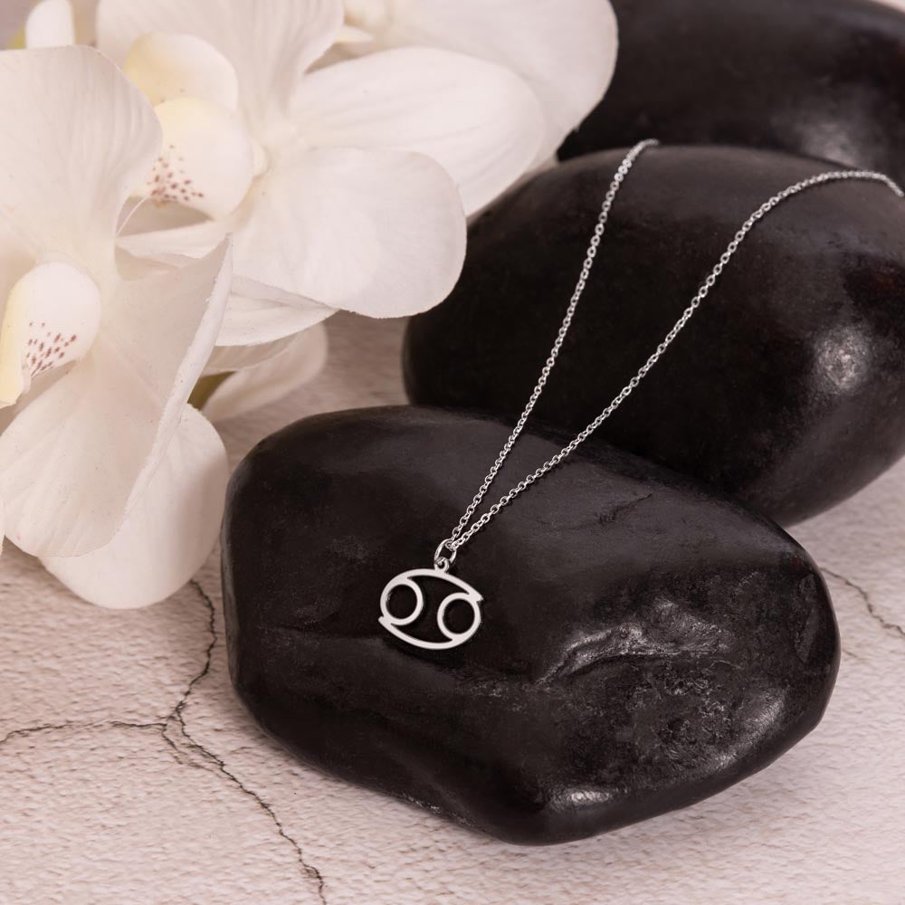 Cancer Zodiac Symbol Necklace for Girls – A Meaningful Gift for a Cancer Girl | Stainless Steel or 18k Yellow Gold Finish displayed on black stones with white flowers