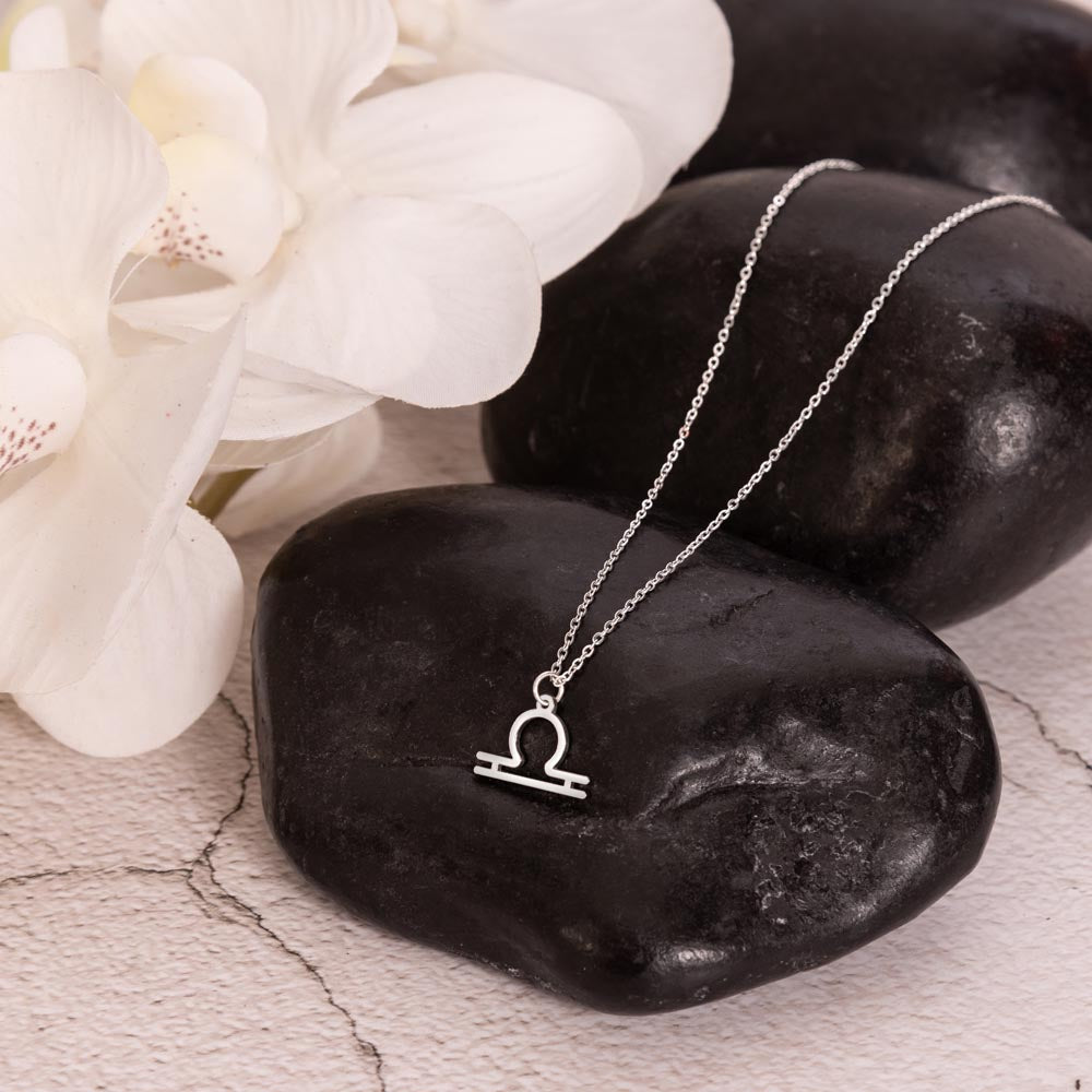 Libra Zodiac Necklace for Women – Astrology Gift with silver symbol pendant displayed on black stones beside white orchids