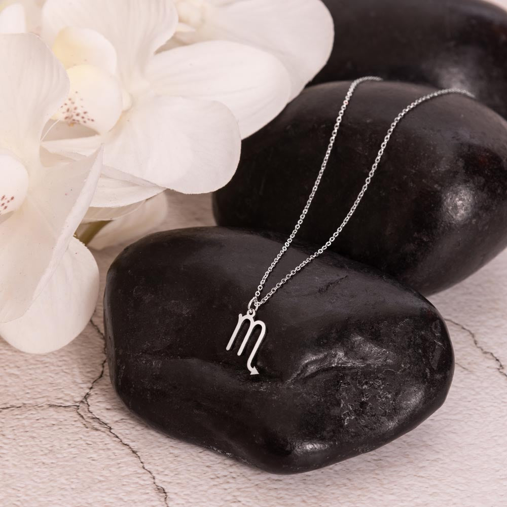 Scorpio Zodiac Symbol Necklace for Girls – A Meaningful Gift for a Scorpio Girl | Stainless Steel or 18k Yellow Gold Finish displayed on black stones with white orchids