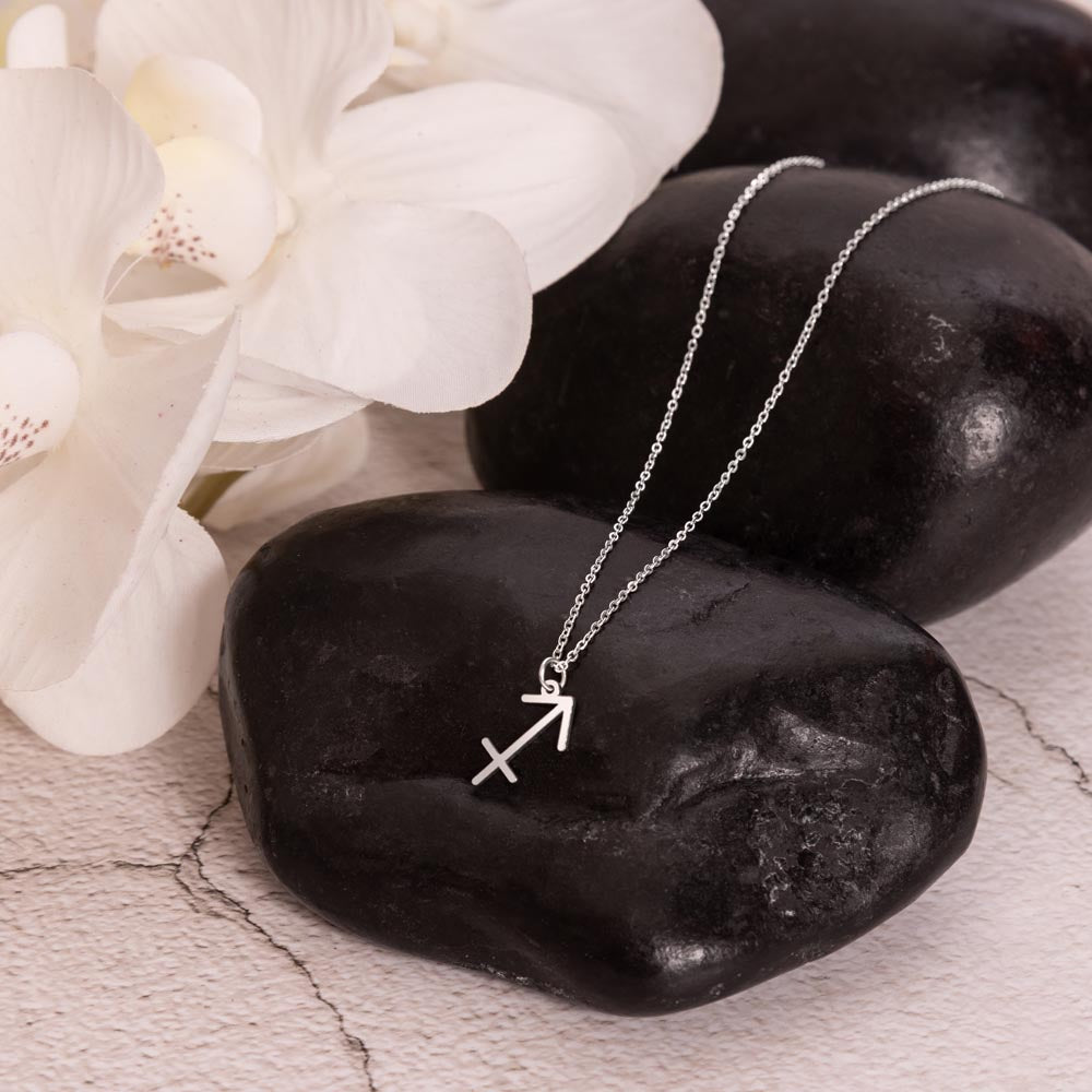 Sagittarius Zodiac Symbol Necklace for Girls – A Meaningful Gift for a Sagittarius Girl | Stainless Steel or 18k Yellow Gold Finish displayed on black stones with white flowers
