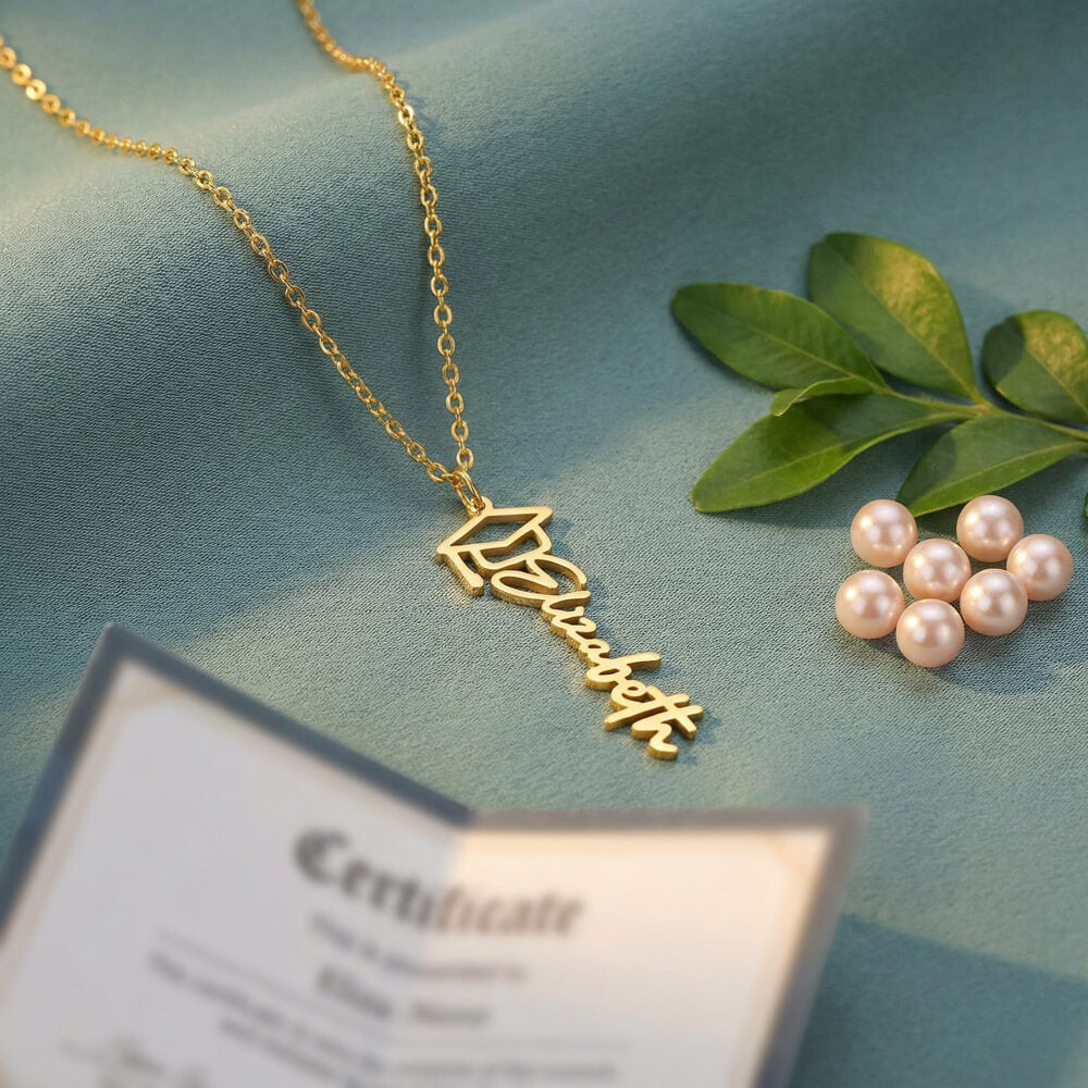 Custom Graduation Cap Name Necklace for Graduate – Personalized Graduation Gift in gold with green leaves and pearls nearby